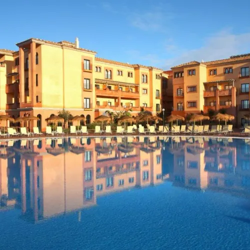 Taxi de Huelva al Barceló Punta Umbría Beach Resort, en Punta Umbría: la piscina y la fachada ocre del hotel, reflejadas en el agua