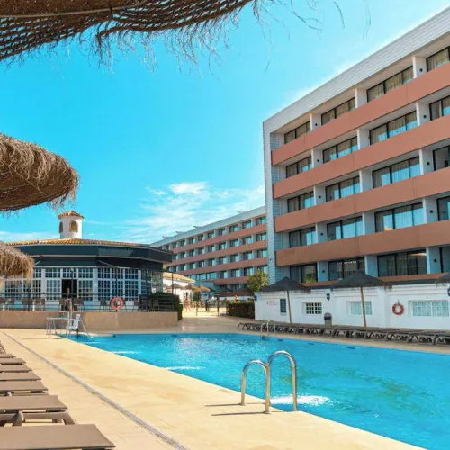 Taxi de Huelva al Ohtels Carabela Beach & Golf, en Matalascañas: la piscina con las sombrillas de paja, junto al edificio del hotel